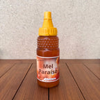 Bottle of Mel Paraíso natural honey with a yellow squeeze cap on a wooden surface.
