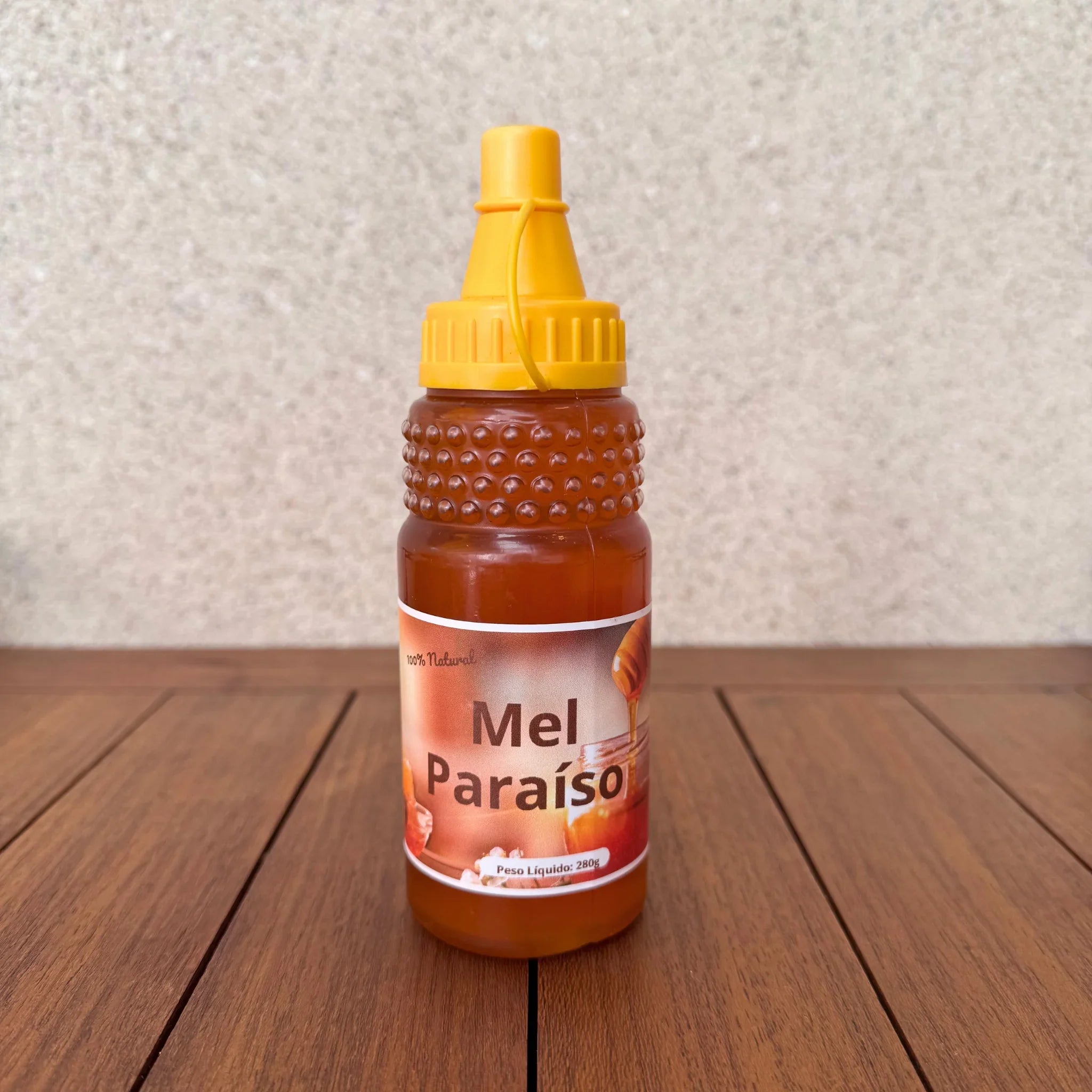 Bottle of Mel Paraíso natural honey with a yellow squeeze cap on a wooden surface.