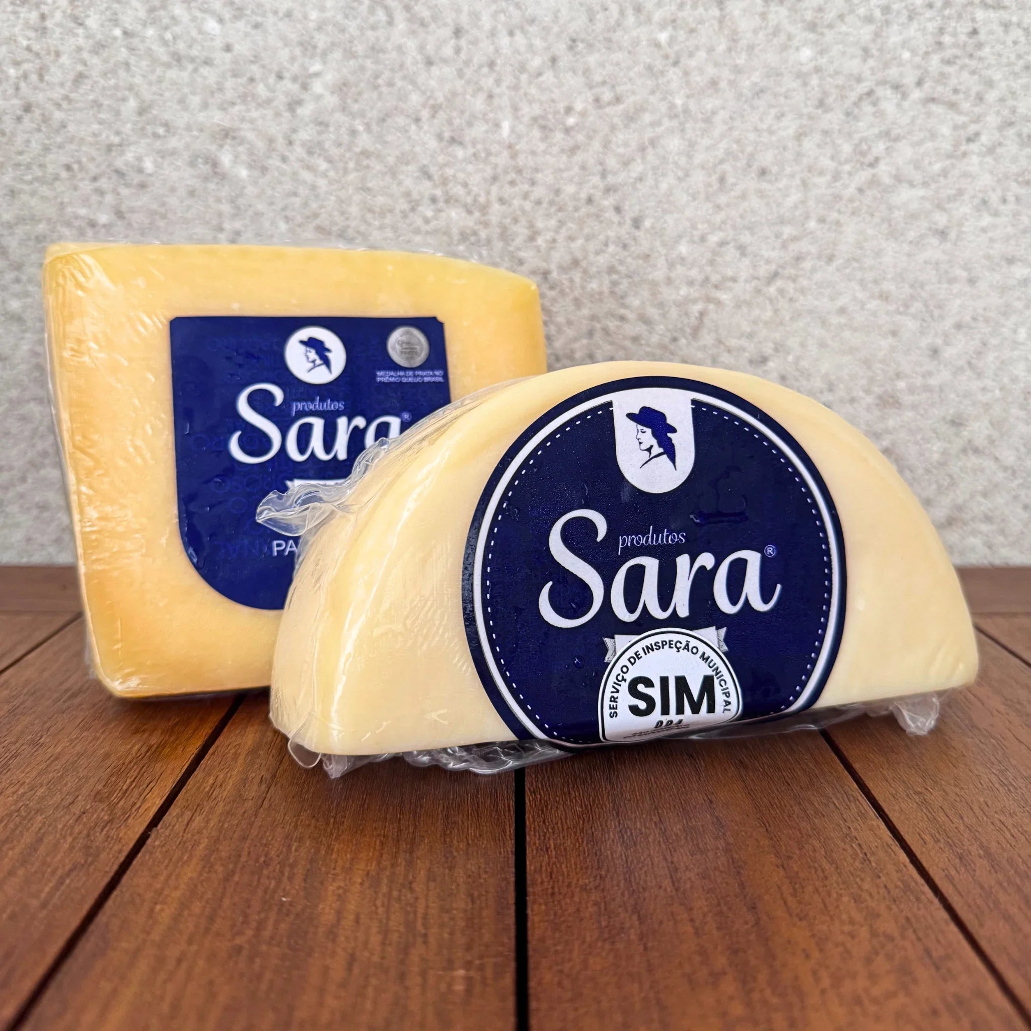 Two wedges of artisanal Sara cheese wrapped in plastic on a wooden surface.