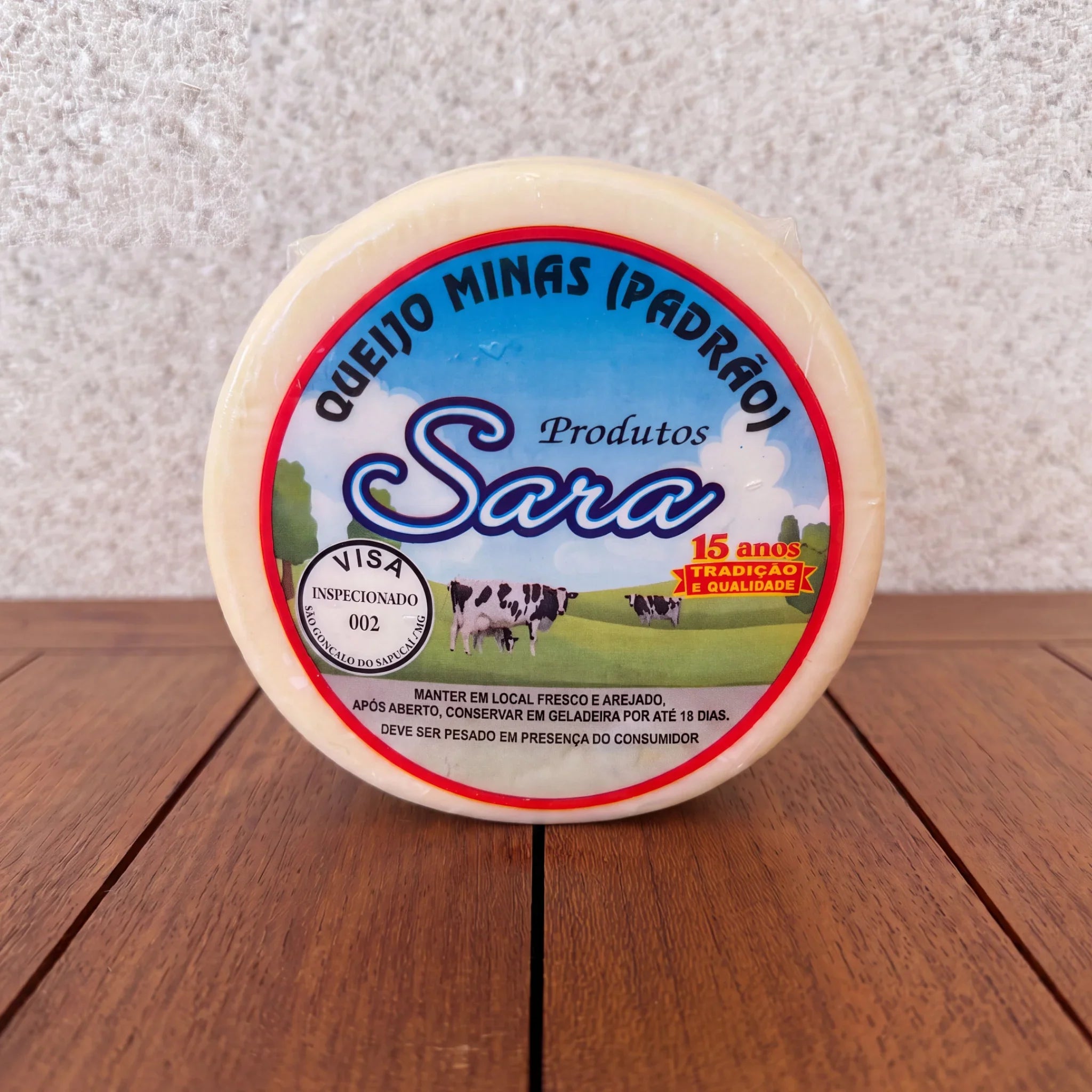 Round wheel of Queijo Minas Padrão from Produtos Sara on a wooden surface.