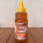 Bottle of Mel Paraíso natural honey with a yellow squeeze cap on a wooden surface