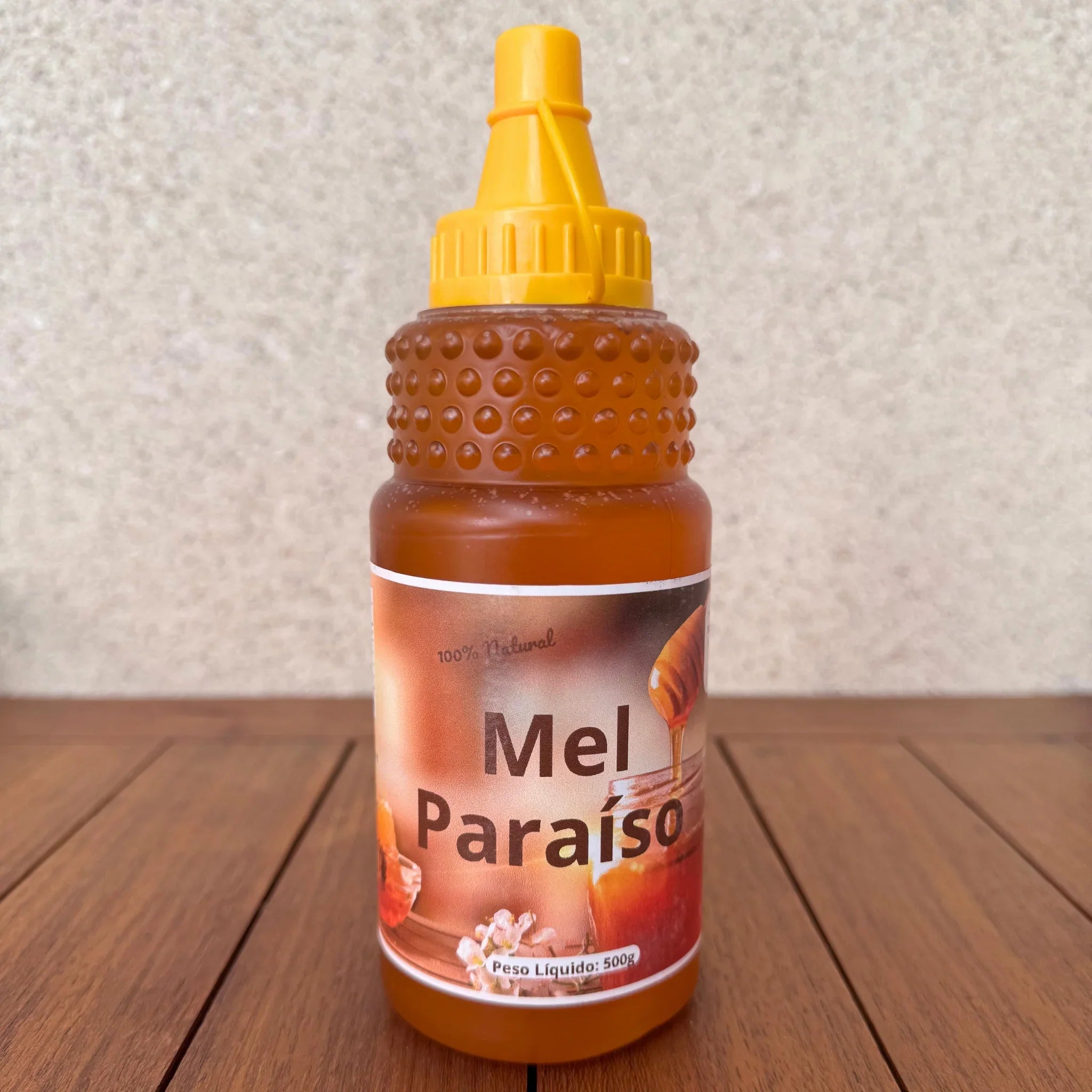 Bottle of Mel Paraíso natural honey with a yellow squeeze cap on a wooden surface